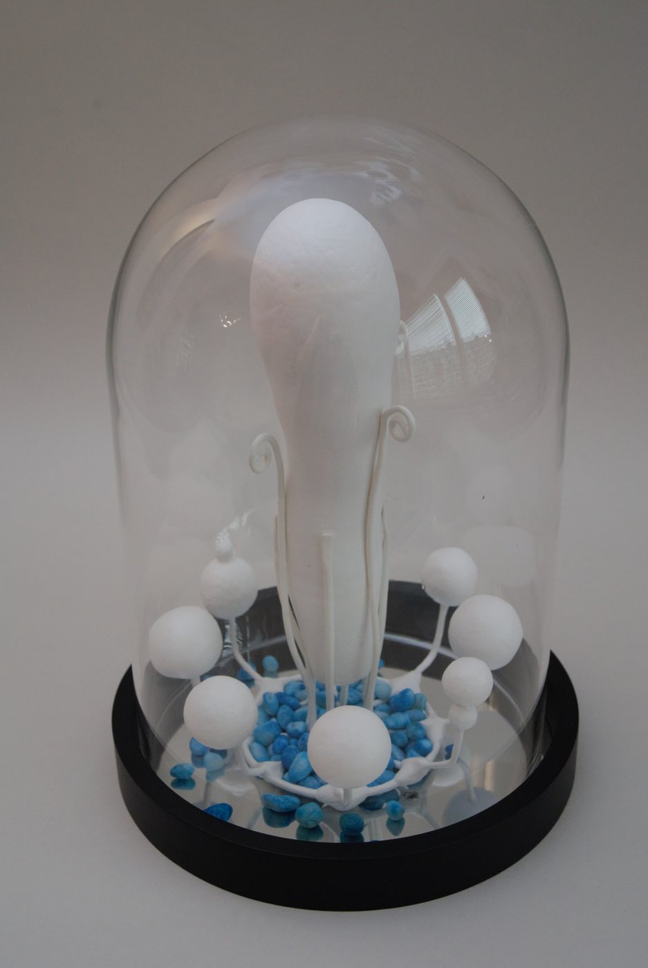 Z.T., 2025 - under a glass dome, a white bulbous glass form rising from a bed of small white spheres and blue fragments.
